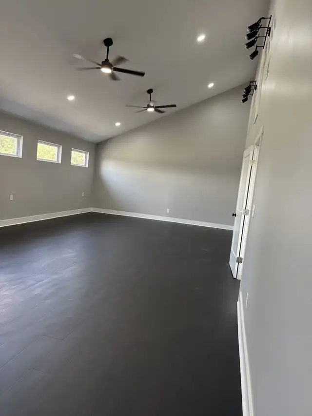 Finished room with dark plank flooring, gray walls, vaulted ceiling and ceiling fan