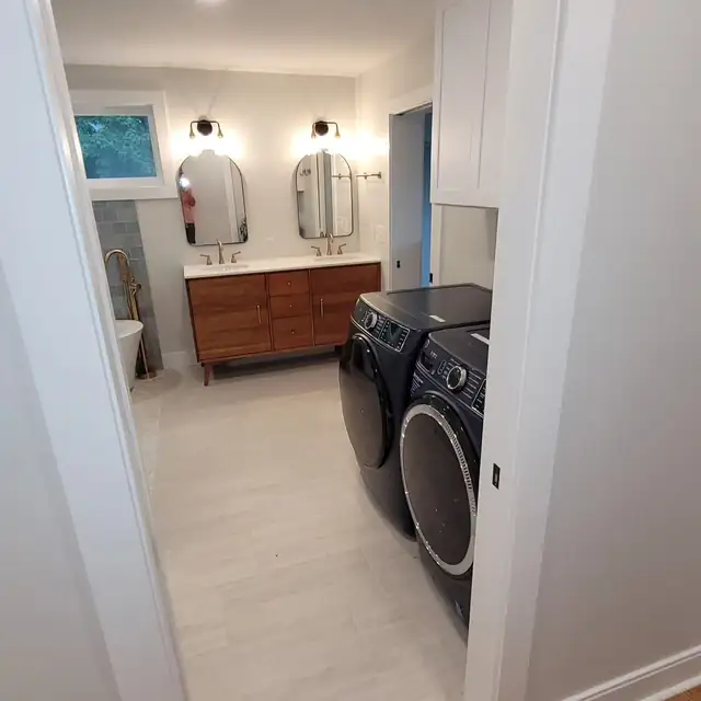 Bathroom with a wood double vanity, two oval mirrors, light plank tile floor and a stacked washer and dryer