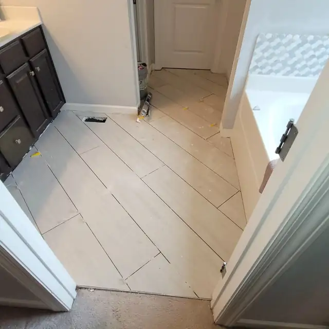New large-format light plank tile floor in a bathroom next to a dark wood door