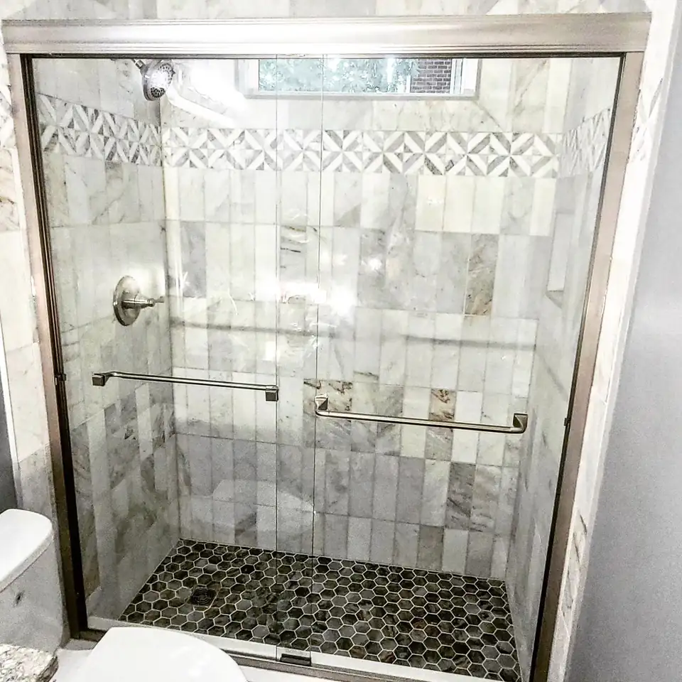 Walk-in shower with white marble-look wall tile, a geometric mosaic band, dark hexagon floor and sliding glass doors, from Forney Home Services, bathroom remodeling in Mt. Juliet